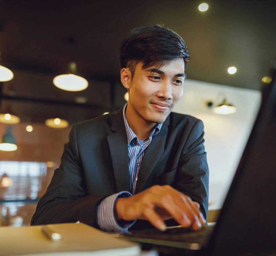 Smiling asian businessman in suit working with laptop