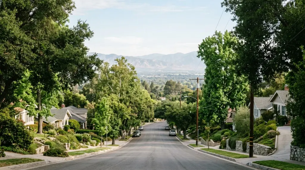 A view looking down a foothill street in Glendora, showcasing mature trees and a glimpse of the distant valley, bathed in soft morning light.