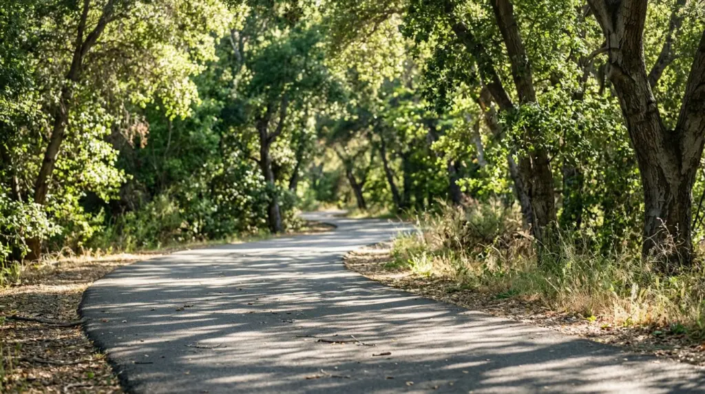 Close-up of a segment of the Pacific Electric Trail, with dappled sunlight filtering through mature trees onto the paved path.